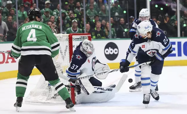 Winnipeg Jets goaltender Connor Hellebuyck (37) blocks a shot as center Mason Appleton (22) helps against pressure from Dallas Stars defenseman Miro Heiskanen (4) in the first period of Game 6 of a second-round NHL hockey playoff series in Dallas, Saturday, May 17, 2025. (AP Photo/Gareth Patterson)