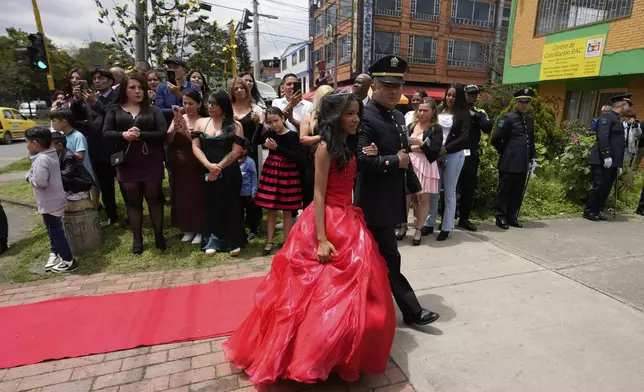 A quinceañera is escorted by a police officer as part of her celebration, in Bogota, Colombia, Friday, May 2, 2025. The Sueños Hechos Foundation, led by a former police officer, is hosting a quinceañera celebration on Friday for 24 disadvantaged teen girls. (AP Photo/Fernando Vergara)