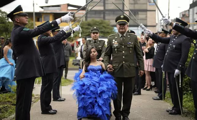 A quinceañera is escorted by a police officer as part of her celebration, in Bogota, Colombia, Friday, May 2, 2025. The Sueños Hechos Foundation, led by a former police officer, is hosting a quinceañera celebration on Friday for 24 disadvantaged teen girls. (AP Photo/Fernando Vergara)