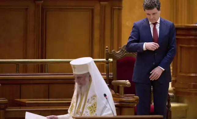 Romania’s newly elected president Nicusor Dan makes the sign of the cross as Patriarch Daniel, the head of Romania's orthodox church, finishes reading a blessing during a swearing in ceremony for the country's new president at the parliament in Bucharest, Romania, Monday, May 26, 2025. (AP Photo/Vadim Ghirda)