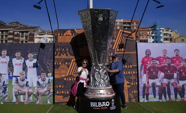Fans pose for a photo next to a giant replica of the Europa League trophy ahead of the final soccer match between Tottenham Hotspur and Manchester United at the San Mamés Stadium in Bilbao, Spain, Wednesday, May 21, 2025. (AP Photo/Manu Fernandez)