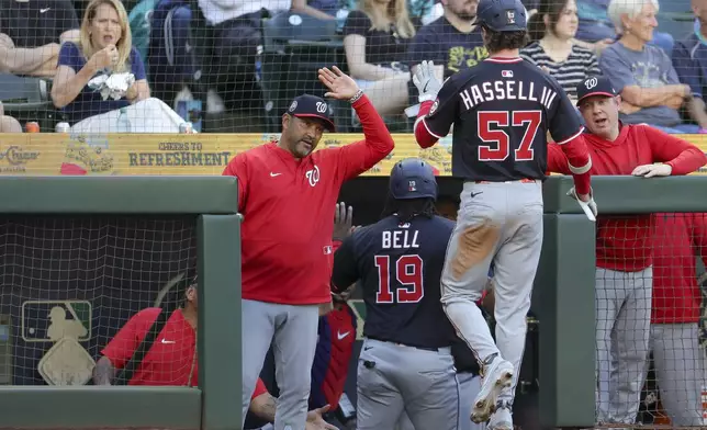 Washington Nationals manager Dave Martinez high fives Robert Hassell III after he scored off a double hit by Jose Tena during the fourth inning of a baseball game against the Seattle Mariners Wednesday, May 28, 2025, in Seattle. (AP Photo/Ryan Sun)