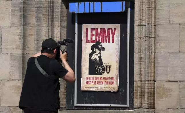 A photographer takes a picture of a poster of singer Lemmy Kilmister which is on display to commemorate the Motorhead frontman in Burslem, Stoke on Trent, England, Friday, May 9, 2025. The musician, once described as having 'one of the most recognizable voices in rock', was born in Burslem and a statue has been crafted by acclaimed local sculptor and lifelong Motorhead fan Andy Edwards. (AP Photo/Kirsty Wigglesworth)