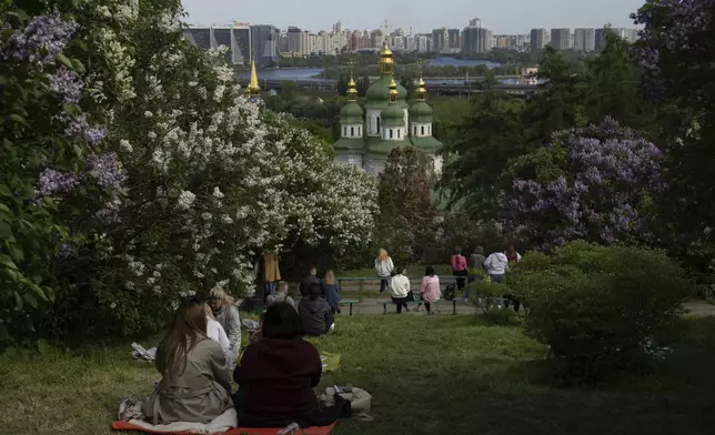 People enjoy the flourishing lilac sitting on the slopes above the Dnipro river near the thousand-year Vydubetsky Monastery in the Botanic Garden in Kyiv, Ukraine, Monday, April 28, 2025.