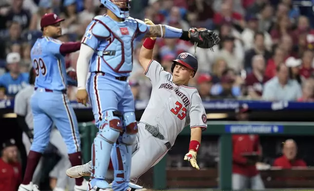 Washington Nationals' Nathaniel Lowe, right, scores past Philadelphia Phillies catcher Rafael Marchán after a fielding error by first baseman Bryce Harper on a batted ball by Keibert Ruiz during the sixth inning of a baseball game, Thursday, May 1, 2025, in Philadelphia. (AP Photo/Matt Slocum)