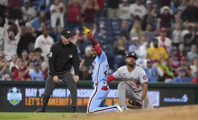 Philadelphia Phillies' Johan Rojas, center, reacts past Washington Nationals third baseman José Tena after hitting a triple during the ninth inning of a baseball game, Thursday, May 1, 2025, in Philadelphia. (AP Photo/Matt Slocum)