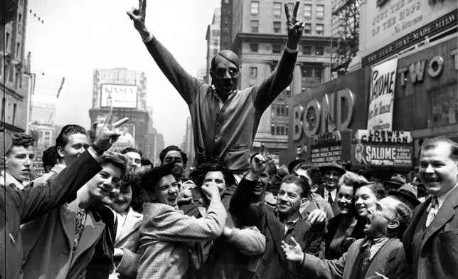FILE - New Yorkers gather around a youth wearing a mask of Adolf Hitler to cheer the news of the surrender of Germany in New York's Times Square on May 7, 1945. (AP Photo/Harry Harris, File)