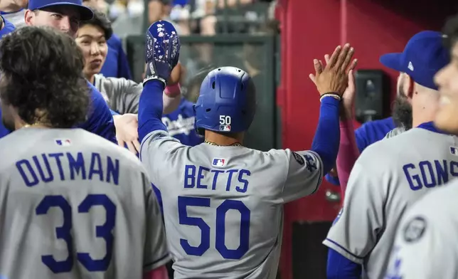 Los Angeles Dodgers shortstop Mookie Betts (50) gets high-fives from teammates after scoring during the fifth inning of a baseball game against the Arizona Diamondbacks, Sunday, May 11, 2025, in Phoenix. (AP Photo/Darryl Webb)
