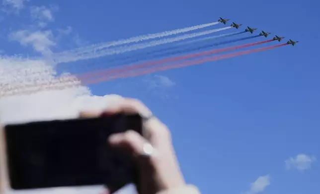 A woman takes pictures as Russian Air Force Su-25 jets fly over Red Square leaving trails of smoke in the colors of Russian state flag during the Victory Day military parade in Moscow, Russia, Friday, May 9, 2025, during celebrations of the 80th anniversary of the Soviet Union's victory over Nazi Germany during the World War II. (AP Photo/Pavel Bednyakov, Pool)