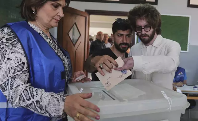 A Hezbollah member who was wounded during Sept. 17, 2024 pager explosions right, casts his vote at a polling station during municipal elections in the town of Nabatieh, south Lebanon, Saturday, May 24, 2025. (AP Photo/Mohammed Zaatari)