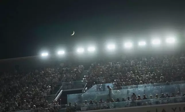 The moon appears over the center court Philippe-Chatrier during the third round match between Spain's Carlos Alcaraz and Bosnia and Herzegovina's Damir Dzumhur at the French Open tennis tournament at the Roland-Garros, Friday, May 30, 2025, in Paris. (AP Photo/Thibault Camus)