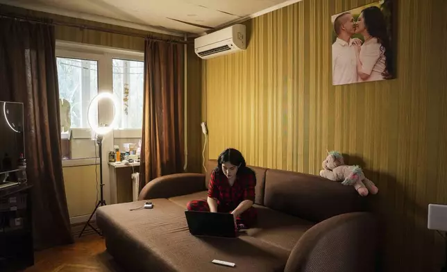 Olha Kurtmalaieva works with a computer sitting on a sofa at her apartment in Kyiv, Ukraine, on Tuesday, June 17, 2025. (AP Photo/Evgeniy Maloletka)