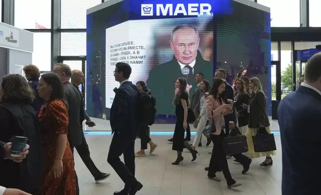 Guests and participants walk in front of a TV screen showing Russian President Vladimir Putin on the sidelines of the St. Petersburg International Economic Forum in St. Petersburg, Russia, Wednesday, June 18, 2025. (AP Photo/Dmitri Lovetsky)
