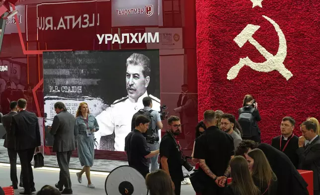 Guests and participants walk in front of an image of Soviet Leader Josef Stalin and a Soviet symbol on the sidelines of the St. Petersburg International Economic Forum in St. Petersburg, Russia, Wednesday, June 18, 2025. (AP Photo/Dmitri Lovetsky)