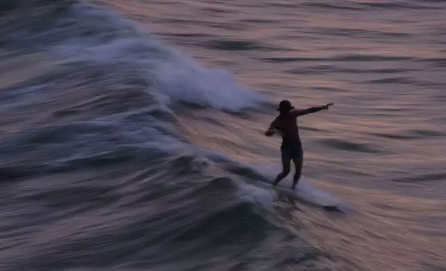 A surfer catches a wave as the color of the sunset sky is reflected on the water Tuesday, June 17, 2025, in Navarre Beach, Fla. (AP Photo/Kiichiro Sato)