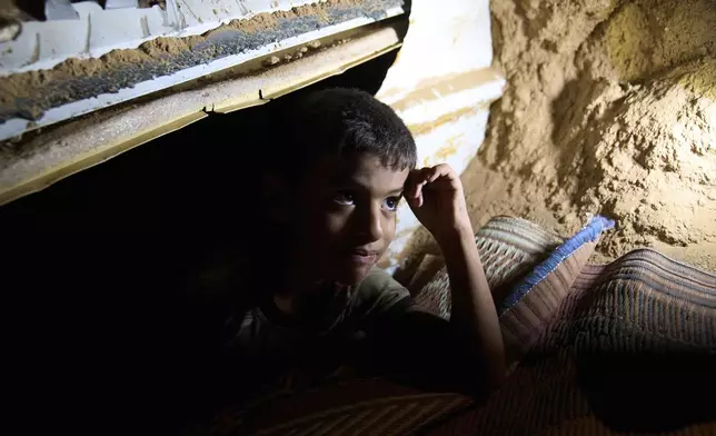 Mohammed Abu Ganima, 7, peers out of a makeshift shelter in his Bedouin village: a minibus buried in the earth to try to protect his family from incoming Iranian fire, in the Negev Desert in southern Israel, early Wednesday, June 18, 2025. (AP Photo/Maya Alleruzzo)