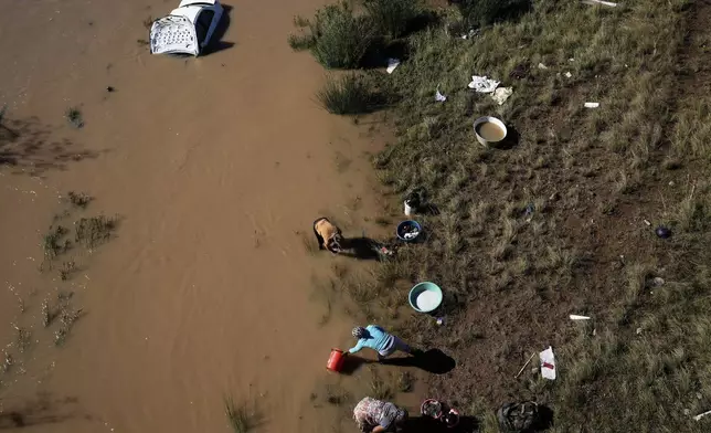 Women wash their clothes along the river next a car that was swept through by floods in Mthatha, South Africa, Thursday, June 12, 2025. (AP Photo/Themba Hadebe)