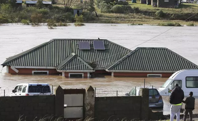 A man with a child look at a home submerged in floodwater, in Mthatha, South Africa, Tuesday, June 10, 2025. (AP Photo/Hoseya Jubase)