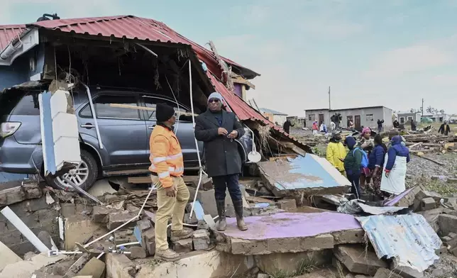 Eastern Cape premier Oscar Mabuyane, center stands with a local government official stand in front of a damaged home after flooding in the area, in Mthatha, South Africa, Wednesday, June 11, 2025. (AP Photo)