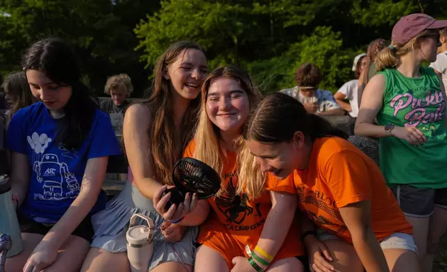 FILE - Mirabelle Demske, second from left, uses a portable electric fan to cool off her friends Faith Hamzy, center, and Annie Sayre, second from right, June 20, 2024, at YMCA Camp Kern in Oregonia, Ohio. (AP Photo/Joshua A. Bickel, File)