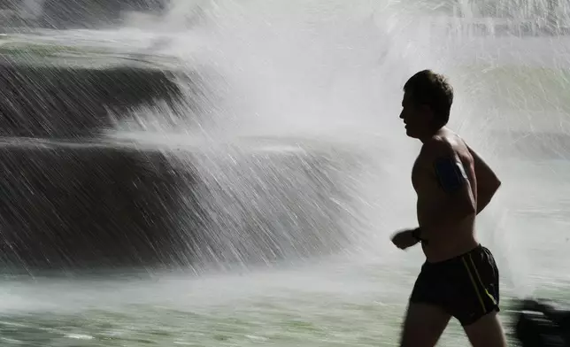 A man runs past a fountain as temperatures approach 100 degrees, Friday, June 20, 2025, in Kansas City, Mo. (AP Photo/Charlie Riedel)