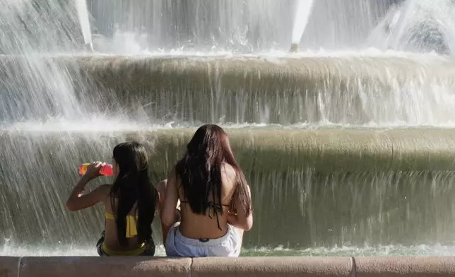 Kids cool off in the mist from a fountain as temperatures approach 100 degrees, Friday, June 20, 2025, in Kansas City, Mo. (AP Photo/Charlie Riedel)