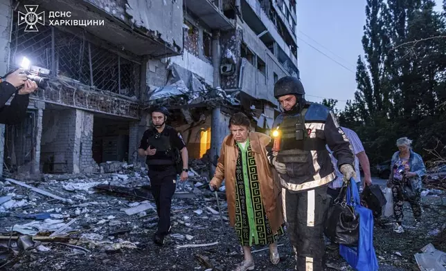 In this photo provided by the Ukrainian Emergency Services on Thursday, June 12, 2025, a rescue worker evacuates a woman from a building which was damaged by a Russian strike in Kharkiv, Ukraine. (Ukrainian Emergency Services via AP)