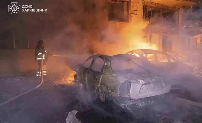 In this photo provided by the Ukrainian Emergency Services on Thursday, June 12, 2025, a rescue worker puts out a fire of a car near a building which was damaged by a Russian strike in Kharkiv, Ukraine. (Ukrainian Emergency Services of Ukraine via AP)