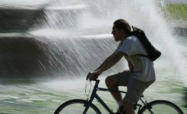A cyclist rides past a fountain as temperatures approach 100 degrees, Friday, June 20, 2025, in Kansas City, Mo. (AP Photo/Charlie Riedel)
