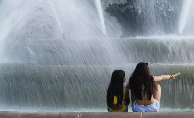 Kids cool off in the mist from a fountain as temperatures approach 100 degrees, Friday, June 20, 2025, in Kansas City, Mo. (AP Photo/Charlie Riedel)