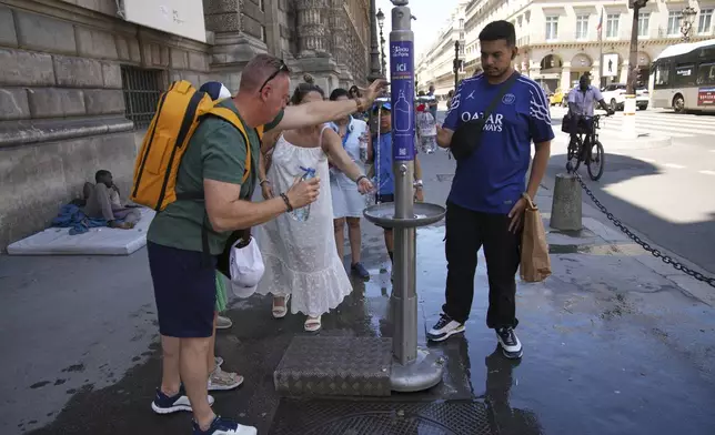 People use a street water fountain during a heat wave, Monday, June 30, 2025 in Paris. (AP Photo/Christophe Ena)