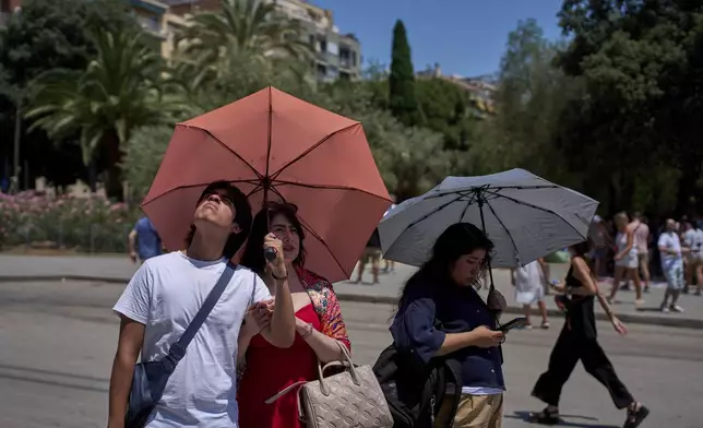 Tourists protect themselves from the sun with umbrellas while looking at the Sagrada Familia church on a hot day in Barcelona, Spain, Monday, June 30, 2025. (AP Photo/Emilio Morenatti)
