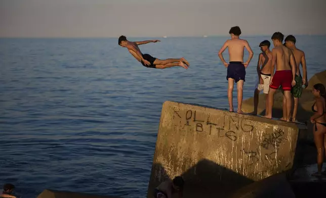 Young swimmers jump into the water from a rock on a breakwater on a hot day in Barcelona, Spain, Sunday, June 29, 2025. (AP Photo/Emilio Morenatti)