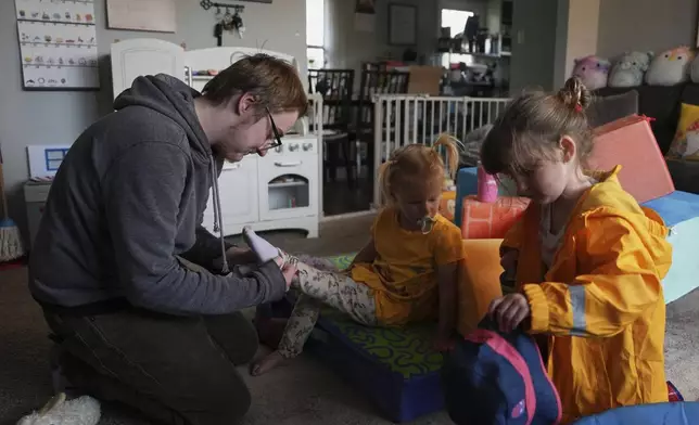 Kirt Ethridge, left, puts socks on his daughter, Naomi, 2, center, as his other daughter, Eliza, 5, gets a hat before a walk Thursday, April 10, 2025, in Evansville, Ind. (AP Photo/Joshua A. Bickel)