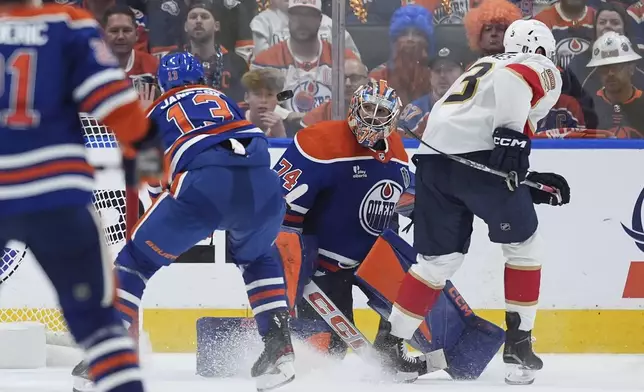 Edmonton Oilers goalie Stuart Skinner (74) makes the save while being screened by Florida Panthers' Seth Jones (3) as Edmonton's Mattias Janmark (13) defends during the first overtime period in Game 2 of the NHL Stanley Cup Final, in Edmonton, Alberta, Friday, June 6, 2025. (Darryl Dyck/The Canadian Press via AP)