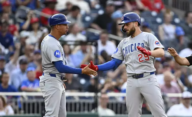 Chicago Cubs' Michael Busch (29) is greeted by third base coach Quintin Berry after hitting a triple against Washington Nationals pitcher Trevor Williams during the second inning of a baseball game in Washington, Tuesday, June 3, 2025. (AP Photo/Terrance Williams)