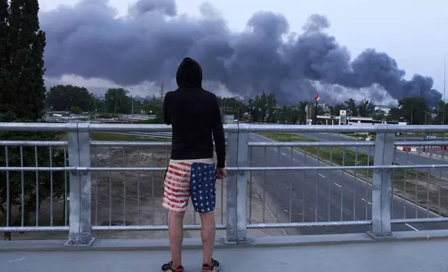 A man watches the burning city following Russia's massive missile and drone attack in Kyiv, Ukraine, Tuesday, June 10, 2025. (AP Photo/Efrem Lukatsky)