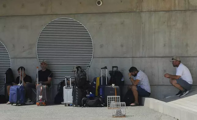 Israelis seek out shade outside the departures terminal at Cyprus' main port in Limassol where they'll board the Israeli cruise ship Crown Iris to take them back to their homeland, on Thursday, June 19, 2025. (AP Photo/Petros Karadjias)