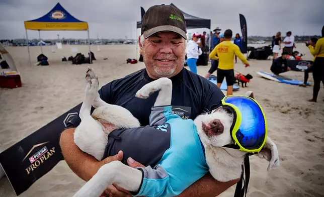 James Will cradles Faith, a 13-year-old partially blind and deaf American pit bull terrier, prior to competing in the annual Incredible Dog Challenge western regional surfing competition in Huntington Beach, Calif., Friday, June 20, 2025. (AP Photo/Richard Vogel)