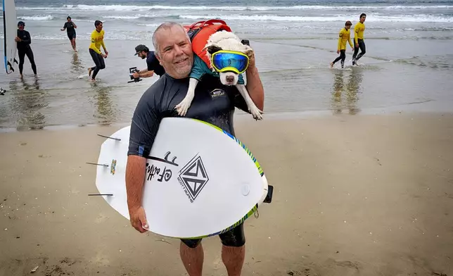 James Will carries his dog Faith, a 13-year-old partially blind and deaf American pit bull terrier, after competing in the annual Incredible Dog Challenge western regional surfing competition in Huntington Beach, Calif., Friday, June 20, 2025. (AP Photo/Richard Vogel)