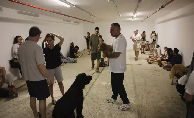 People take shelter as a siren sounds a warning following a missiles that were launched from Iran, in Tel Aviv, Israel, on Friday, June 13, 2025. (AP Photo/Tomer Appelbaum)