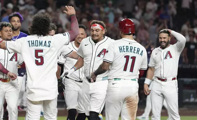 Arizona Diamondbacks' Josh Naylor, center, arrives at home plate to celebrate his walk off grand slam against the Seattle Mariners with Diamondbacks' Eugenio Suárez, right, Jose Herrera (11), Alek Thomas (5) and others during the 11th inning of a baseball game Monday, June 9, 2025, in Phoenix. (AP Photo/Ross D. Franklin)