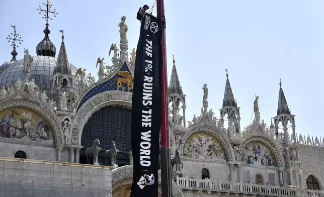 An activist from Extinction Rebellion unfolds a banner in front of St. Mark's Basilica in Venice, Italy, on Thursday, June 26, 2025, ahead of festivities in the lagoon city reportedly linked to a wedding celebration for Jeff Bezos and Lauren Sánchez. (AP Photo/Luigi Costantini)