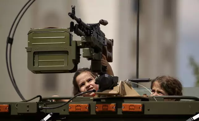 Children touch a machine gun as they climb inside a transporter outside Romania's Palace of Parliament during a series of events marking International Children's Day in Bucharest, Romania, Sunday, June 1, 2025. (AP Photo/Andreea Alexandru)