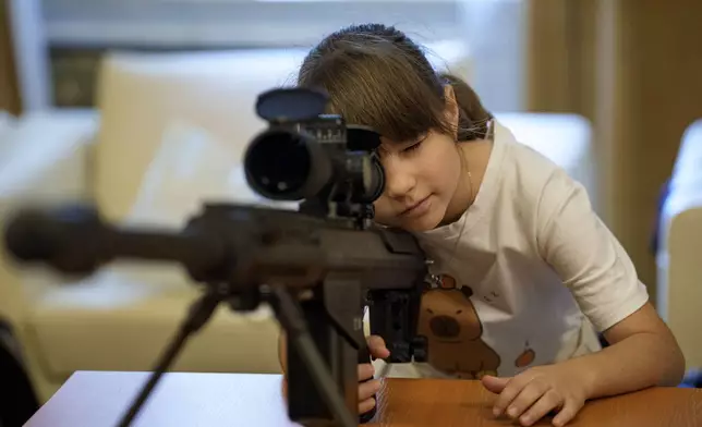 A girl looks through the scope of a military firearm at an exhibition inside Romania's Palace of Parliament during a series of events marking International Children's Day in Bucharest, Romania, Sunday, June 1, 2025. (AP Photo/Andreea Alexandru)