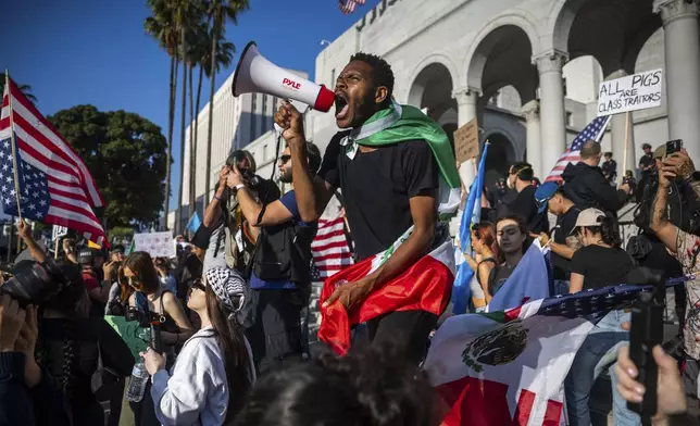 A man shouts into a megaphone outside City Hall during protests over federal immigration enforcement raids on Wednesday, June 11, 2025, in Los Angeles. (AP Photo/Ethan Swope)