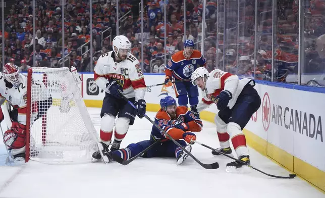 Edmonton Oilers' Leon Draisaitl, center, reaches for the puck after being checked to the ice behind Florida Panthers goalie Sergei Bobrovsky (72) as Aleksander Barkov (16) and Evan Rodrigues (17) defend during the first overtime period in Game 2 of the NHL Stanley Cup Final, in Edmonton, Alberta, Friday, June 6, 2025. (Darryl Dyck/The Canadian Press via AP)