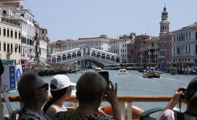 Tourists snap photographs of the Rialto bridge along the Grand Canal in Venice, Italy, on Wednesday, June 25, 2025, ahead of festivities in the lagoon city reportedly linked to a wedding celebration for Jeff Bezos and Lauren Sánchez. (AP Photo/Luca Bruno)