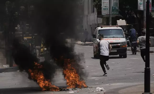 Palestinians run past burning tires during clashes with Israeli forces following a military raid in the West Bank city of Nablus, Tuesday, June 10, 2025. (AP Photo/Majdi Mohammed)