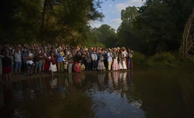 Pilgrims stand on the shore of the Quema River near Aznalcazar, Spain, a crucial point in the annual Catholic pilgrimage to the shrine of the Virgin of El Rocio that draws hundreds of thousands of faithful, Friday, June 6, 2025. (AP Photo/Emilio Morenatti)